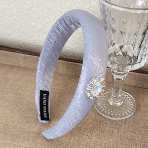 Detail view of light blue padded headband with shiny fabric and jeweled accents