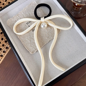 Detail of elegant cream satin bow hair tie with large white pearl drop on linen tray