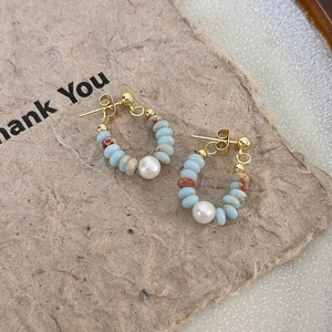 Detailed shot of hoop earrings with light blue beads, brown stones, and white pearls on gold pins