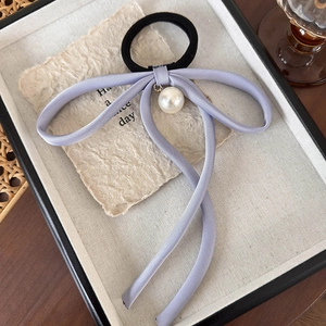 Detail of lavender bow hair tie with a round pearl pendant on a textured paper background
