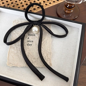 Close-up of black silk ribbon bow hair tie with a round white pearl pendant detail