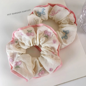 Detail view of cotton hair scrunchies with pink embroidered cherries and bow designs