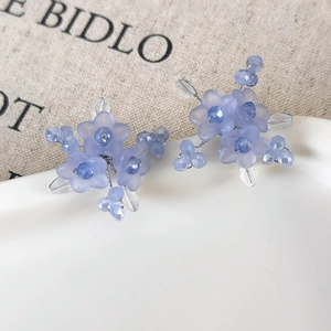 Elegant misty blue floral stud earrings with handcrafted beaded details on white ceramic