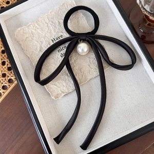 Detail of elegant black satin ribbon bow hair tie with a large white pearl pendant charm