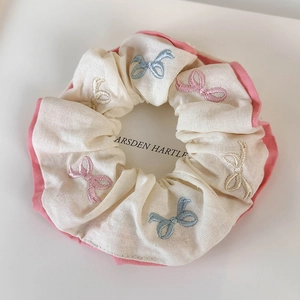 Detail shot of the cotton fabric scrunchie with colorful embroidered bow patterns