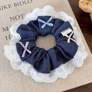 Detail of denim hair scrunchie with white lace edges and three colorful silk bows