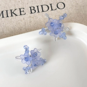 Macro detail of handmade light blue floral earrings with beaded crystals on ceramic tray