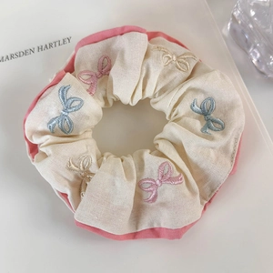 Detail showing cream cotton fabric with delicate pink and blue bow embroidery patterns