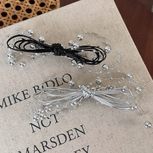 Close-up of woven bow hair clips with silver beads on a textured background