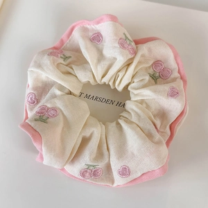 Detail of pink cherry embroidery on cream cotton scrunchie with soft fabric texture