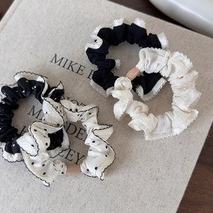 Detailed view of four black and white polka dot scrunchies on a linen book background