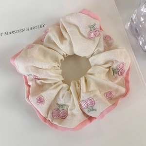 Close-up of cream and pink cotton scrunchie with embroidered cherry and heart patterns