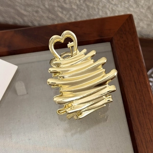 Détail de la pince à cheveux dorée en métal liquide avec poignée en forme de cœur
