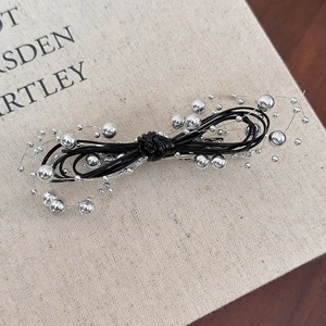 Detail of black bow hair clip with silver beads and wire wrap on linen texture background