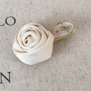 Close-up of handmade cream satin rose hair clip with a pressed flower gold oval charm