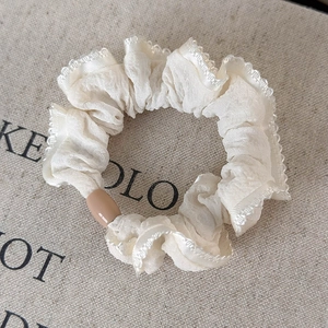 Close-up of cream chiffon hair scrunchie with lace edge and brown cylinder detail