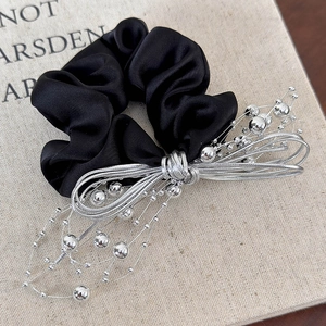 Close-up of black satin hair scrunchie with silver bead bow detail on textured book