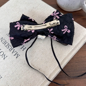 Vue détaillée d'une pince à cheveux noire Y2K avec nœuds roses et pendentif cœur argenté
