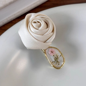 Detailed close-up of cream satin rose hair clip with gold-rimmed floral resin pendant