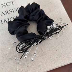 Detail of a black satin scrunchie featuring silver beads and elegant leather cord accents