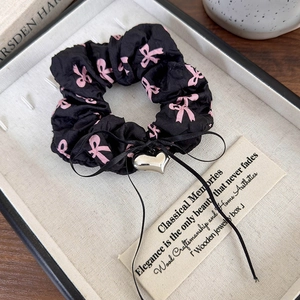 Détail d'un chouchou noir avec motifs de nœuds roses et pendentif cœur dans un coffret