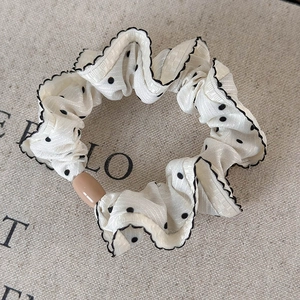 Close-up of cream polka dot hair scrunchie with black wavy edges and a brown bead