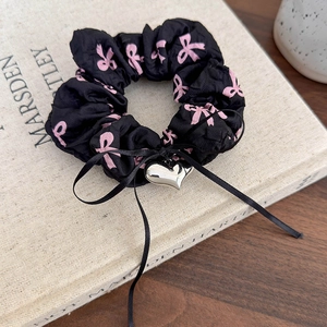 Détail d'un chouchou noir avec imprimés nœuds roses et pendentif cœur en argent