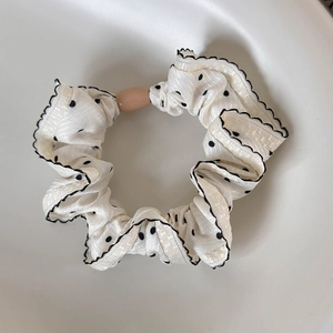 Detailed texture of white polka dot scrunchie with black wave edge in a minimalist tray