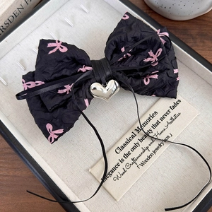 Détail d'un nœud papillon plissé noir avec rubans roses et cœur en métal argent