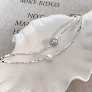 Minimalist double pearl necklace with silver box chain on a decorative shell plate