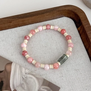 Detail of beaded pink bracelet with green rectangular jade stone in a wood tray