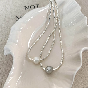 Minimalist silver bead necklace with white and gray pearl pendants on a ceramic shell