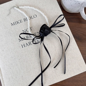 Close-up of elegant black ribbon camellia and white pearl choker with adjustable clasp