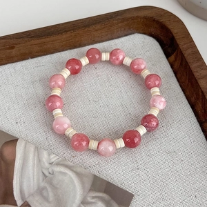 Close-up of pink stone beaded bracelet on textured fabric with wooden tray background