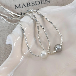 Macro detail of minimalist silver square beads and round pearl pendant on white shell tray