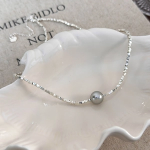 Detail of square silver beads and a gray pearl in a shell-shaped tray with a heart charm