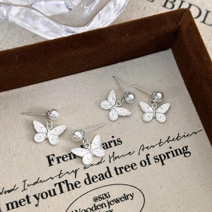 Close-up of silver butterfly stud earrings with hanging white pearls on a vintage background