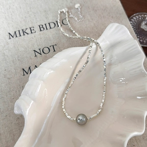 Detail of silver square bead necklace with a gray pearl pendant in a shell tray