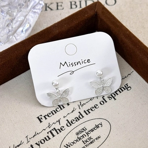 Exquisite silver butterfly pearl earrings on vintage beige fabric and wooden tray