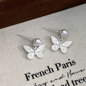 Detail of silver butterfly earrings with white pearls on a textured fabric backdrop