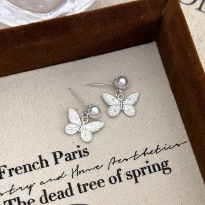 Detailed view of silver butterfly stud earrings with white pearl and textured wings