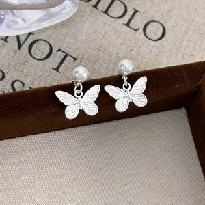 Macro shot of silver butterfly drop earrings with white pearls on a vintage jewelry box