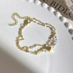 Detailed macro view of double-layer gold chain bracelet with colorful beads and heart charm