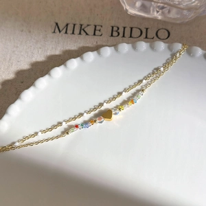 Detail of double-layer gold chain bracelet with colorful beads and heart pendant
