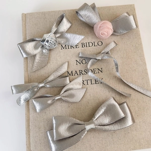 Set of six silver bow hair clips with roses and pink mesh flowers on a beige book