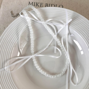 Detail van witte glasparelketting met delicate strikjes op een keramisch dienblad