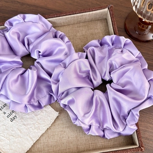 Set of two purple satin ruffle scrunchies on a woven tray for chic hair styling
