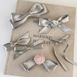 Detail of silver satin bow hair clips featuring metallic rose accents and ribbon textures