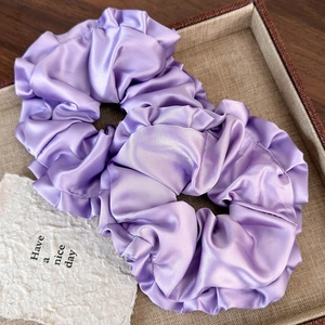 Detail of two large purple satin hair scrunchies with wavy edges on a vintage tray