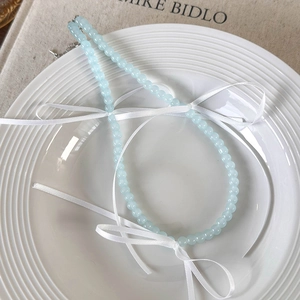 Detail van de lichtblauwe glazen kralenketting met witte strikjes op keramisch bord